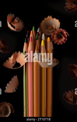 Plan frontal minimaliste d'un groupe de crayons de couleur sur fond noir et d'un groupe de copeaux volant autour. Banque D'Images