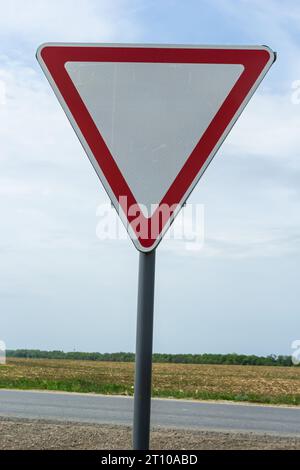 Panneau de signalisation contre le ciel. Triangle blanc avec bordure rouge. Signal, céder. Jour d'été. Banque D'Images