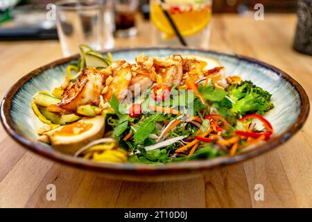 Salade d'herbes asiatiques sucrées et aigres, œufs durs et crevettes avec du piment dans une assiette, boisson dans un verre, dîner sur la table du restaurant. Banque D'Images