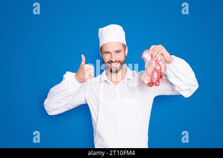 Portrait de boucherie joyeuse gaie avec le chaume ayant de la viande fraîche à la main montrant le signe oui fait à la mode, isolé sur fond gris, publicité Banque D'Images