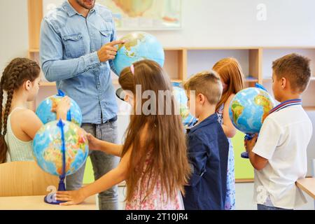 Élèves élémentaires masculins et féminins apprenant par globes en classe de géographie Banque D'Images