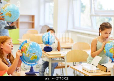 Élèves du primaire examinant les globes pendant la lecture de géographie en classe Banque D'Images