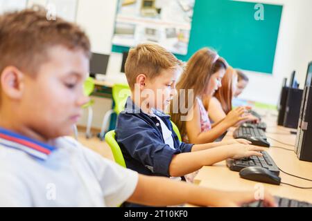 Écolier élémentaire tapant sur le clavier tout en étant assis avec des amis dans la classe d'informatique Banque D'Images