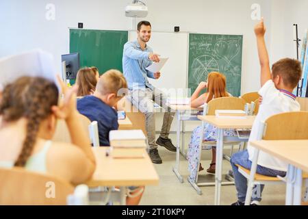 Enseignant souriant pointant du doigt l'élève assis avec la main levée pendant qu'il enseignait en classe Banque D'Images