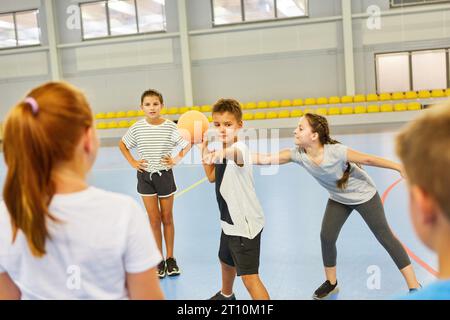 Les écoliers masculins et féminins jouant avec le ballon pendant le cours de gym à l'école Banque D'Images