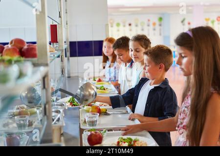 Des élèves souriants, hommes et femmes, prenant de la nourriture tout en faisant la queue pendant la pause déjeuner à la cafétéria de l'école Banque D'Images