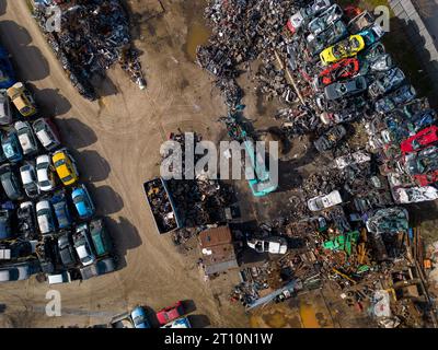 vue aérienne d'une décharge de voiture, où une machine est vue séparant les vieilles voitures en ferraille. La collection massive de voitures abandonnées et la machinerie lourde nous Banque D'Images