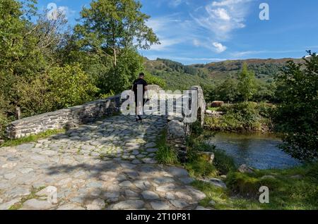 Homme personne marchant sur New Bridge à travers la rivière Derwent Cumbria Way en été Rosthwaite Borrowdale Lake District National Park Cumbria Royaume-Uni Angleterre Banque D'Images