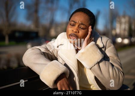 Portrait extérieur de la femme afro-américaine déprimée par temps ensoleillé. Elle est assise sur un banc dans la rue. Banque D'Images