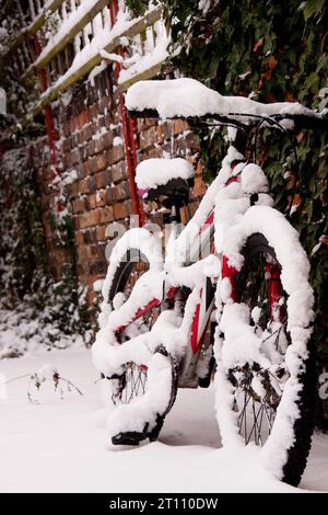 vélo rouge debout dans la neige appuyé contre le mur de briques rouges Banque D'Images