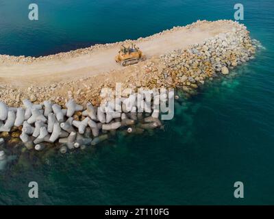 Vue aérienne de dessus de la construction du brise-lames. Bulldozer sur un tas de rochers dans la mer Banque D'Images