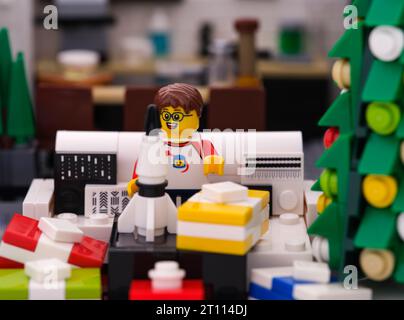 Tambov, Fédération de Russie - 24 septembre 2023 Une minifigurine Lego garçon assis sur un canapé et ouvrant un cadeau avec une fusée jouet à l'intérieur à Noël Banque D'Images