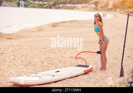 Femme gonflant sup paddle board à l'extérieur avec fond de mer au coucher du soleil Banque D'Images