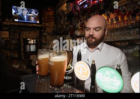 Anthony Geoghegan, directeur du bar, tire des pintes de Guinness dans la maison publique d'O'Donoghue à Dublin, alors que Paschal Donohoe, ministre des dépenses publiques, dévoile le budget du gouvernement pour 2024 à la télévision. Date de la photo : mardi 10 octobre 2023. Banque D'Images