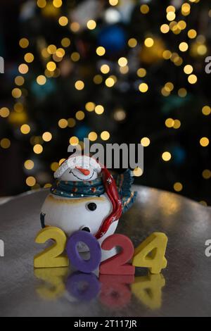 Bonne année 2024 - bonhomme de neige souvenir et chiffres sur fond de guirlande lumineuse jaune, bokeh. en prévision des vacances de noël. C'est l'heure de chan Banque D'Images