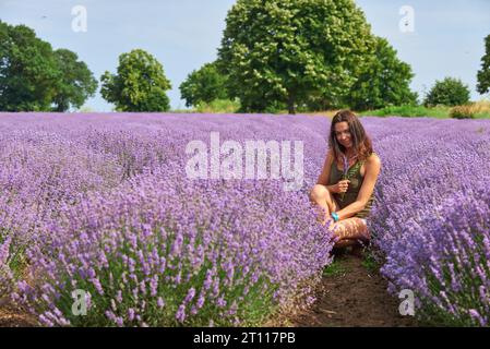 jeune femme en vêtements décontractés marche à travers un champ de lavande en fleurs, des couleurs naturelles Banque D'Images