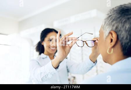 Femme, médecin et optométrie pour les lunettes avec le patient après l'examen des yeux dans l'espace pour la prescription, la santé et le bien-être. Personne mature, nouvelle et lentille par Banque D'Images