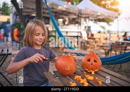 Garçon de 8 ans sculptant la citrouille d'Halloween en plein air à la cour Banque D'Images