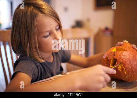 Garçon de 8 ans sculptant la citrouille d'Halloween à la maison Banque D'Images