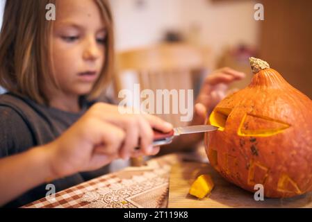 Garçon de 8 ans sculptant la citrouille d'Halloween à la maison Banque D'Images