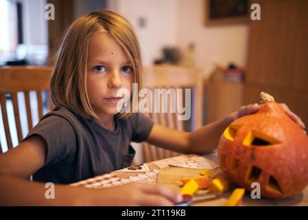 Garçon de 8 ans sculptant la citrouille d'Halloween à la maison Banque D'Images