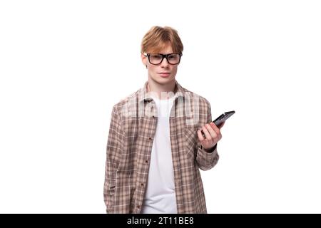 jeune homme caucasien aux cheveux roux dans une chemise utilise activement un smartphone Banque D'Images