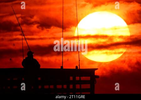 Île de Palms, États-Unis. 10 octobre 2023. Les pêcheurs silhouettes par le lever du soleil alors qu'ils jettent pour le matin à prendre au large de Sea Cabins Pier par un matin froid dans le bas pays, le 10 octobre 2023 à Isle of Palms, Caroline du Sud. Crédit : Richard Ellis/Richard Ellis/Alamy Live News Banque D'Images