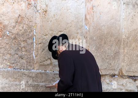 Homme juif au mur des lamentations à jérusalem. Homme dans les vêtements traditionnels se pliant la tête devant les pierres sacrées du mur occidental. Dire des prières et parler à Banque D'Images