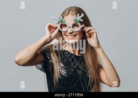 Une jeune femme blonde souriante dans des lunettes avec des bois de cerf isolés sur fond blanc. Concept Noël et nouvel an. Banque D'Images