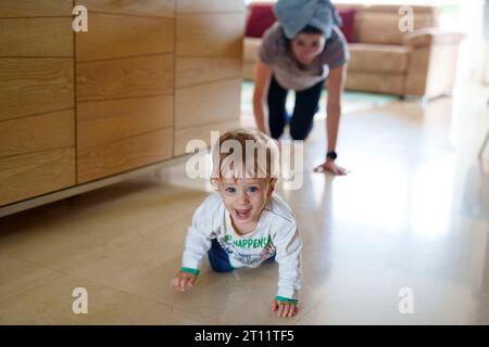 Bébé joyeux rigolant rampant loin de sa mère pendant le temps de jeu à la maison Banque D'Images