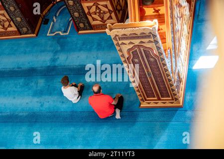 Adulte et enfant prient à l'intérieur de la mosquée avec un tapis bleu Banque D'Images