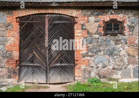 Petite fenêtre figurée et une grande porte fermée en bois menant à la grange en pierre. De la série portes du monde. Banque D'Images