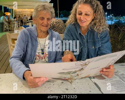 Malia, Crète, Grèce, Europe, 01 OCT 2023. Femmes lisant un menu dans un restaurant grec, Malia, Crète. Banque D'Images