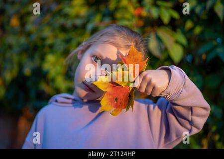 Fille heureuse tient les feuilles d'érable collectées dans ses mains fille jouant avec les feuilles tombées dans le parc d'automne. Saison d'automne Banque D'Images