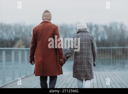 Vue arrière d'un couple de personnes âgées marchant près de la rivière, pendant la froide journée d'hiver. Banque D'Images