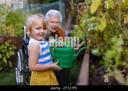 Portrait d'une petite fille adorable aidant sa grand-mère dans le jardin, arrosant les plantes, s'occupe des légumes poussant dans des lits surélevés. Banque D'Images