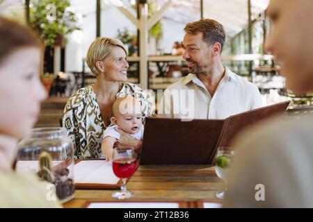 Famille avec des menus de lecture de bébé dans un restaurant, choisir la nourriture et les boissons. Banque D'Images