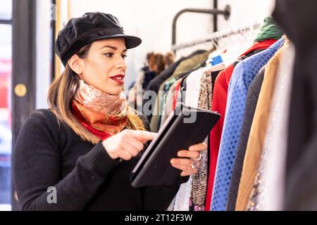 Assistant de magasin Latina faisant l'inventaire avec un magasin de tablettes, d'occasion et de vêtements durables Banque D'Images