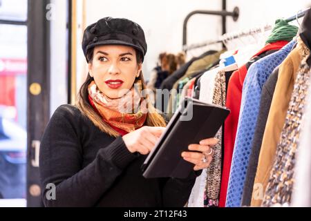 Assistant de magasin Latina faisant l'inventaire avec un magasin de tablettes, d'occasion et de vêtements durables Banque D'Images