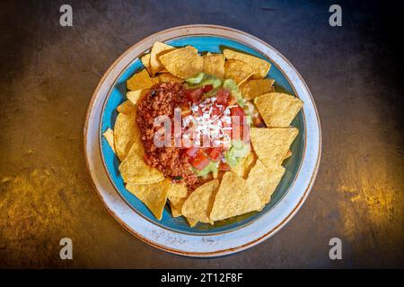 Nachos au guacamole et sauce tomate sur fond noir, sur une assiette bleue Banque D'Images