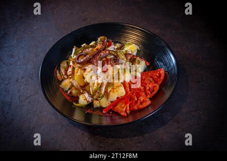 Salade avec pommes de terre et poulpe au paprika épicé sur fond noir, sur une assiette noire Banque D'Images