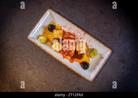 Tentacule de poulpe avec des pommes de terre sur fond noir, sur une assiette blanche Banque D'Images
