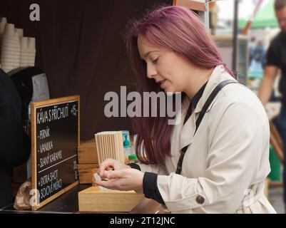 Jolie jeune femme achetant du café et comptant des pièces de monnaie pour vendeur au stand des agriculteurs au marché de rue à Prague. Banque D'Images