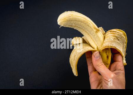 Une banane pelée dans la main d'une femme sur un fond noir Banque D'Images