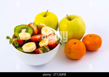 Vue aérienne d'Une salade de fruits coupée dans un bol blanc sur fond blanc à côté de mandarines et de pommes Banque D'Images