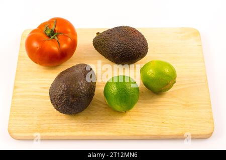 Deux bons avocats, une tomate et deux limes sur un bois. Recette pour faire un bon guacamole Banque D'Images