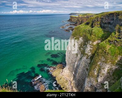 Hautes falaises côtières sur la côte d'Antrim, près de Giant's Causeway, Irlande du Nord. Les ruines du château de Dunluce apparaissent en arrière-plan. Banque D'Images