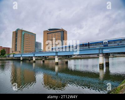 Un train de banlieue local traverse la rivière Lagan près de la gare de Lanyon place à Belfast, en Irlande du Nord, au Royaume-Uni. Le bâtiment BT et l'hôtel Hilton apparaissent Banque D'Images