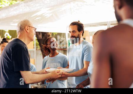 Les membres d'une communauté multiculturelle se réunissent, faisant du bénévolat dans un centre à but non lucratif pour donner de la nourriture et des produits essentiels aux sans-abri et aux défavorisés. De jeunes bénévoles aident les pauvres et les nécessiteux. Banque D'Images