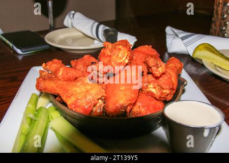 Ailes de bufflonne pillotées dans une petite poêle en fonte sur une table de restaurant avec sauce céleri et fromage bleu. Banque D'Images